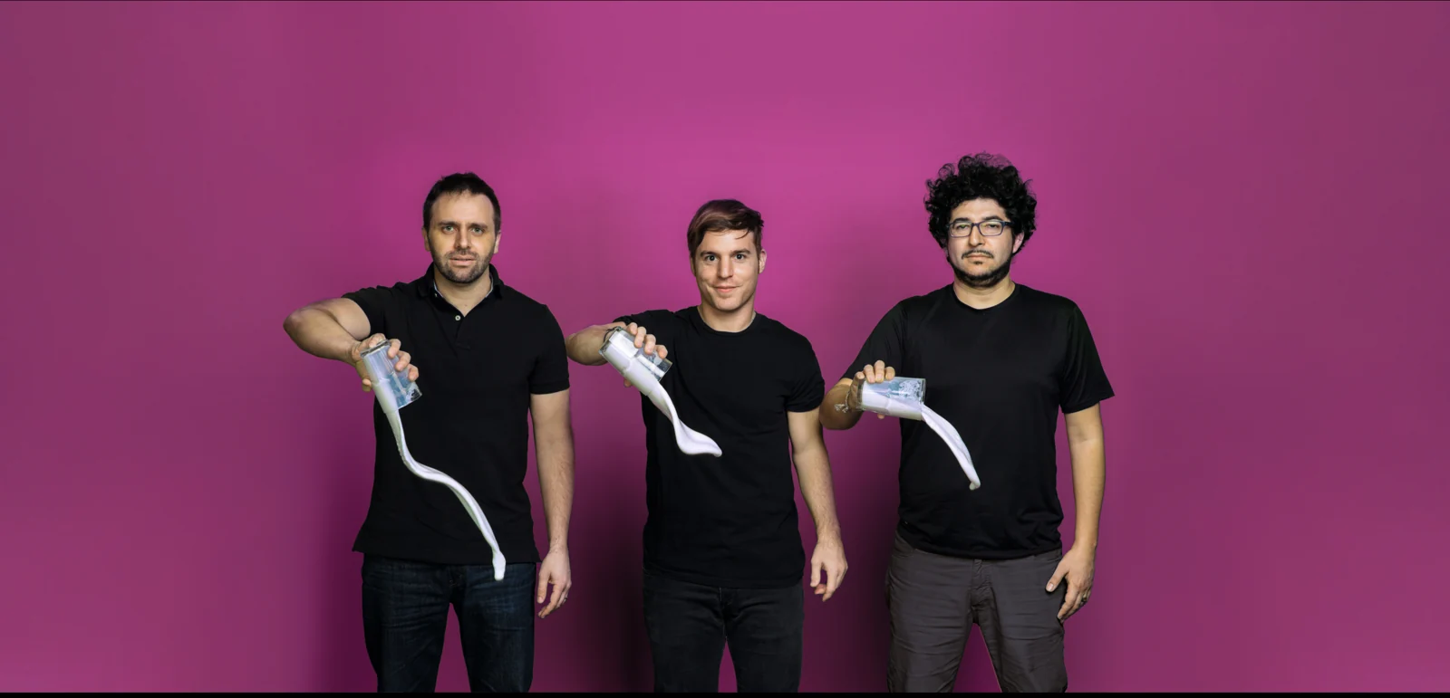 Tres integrantes del equipo fundador de NotCo sostienen vasos con líquido blanco ante un fondo magenta